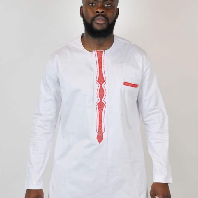 Frontal of model wearing a men's traditional African white shirt with red embroidery panel detail on the front and pocket.