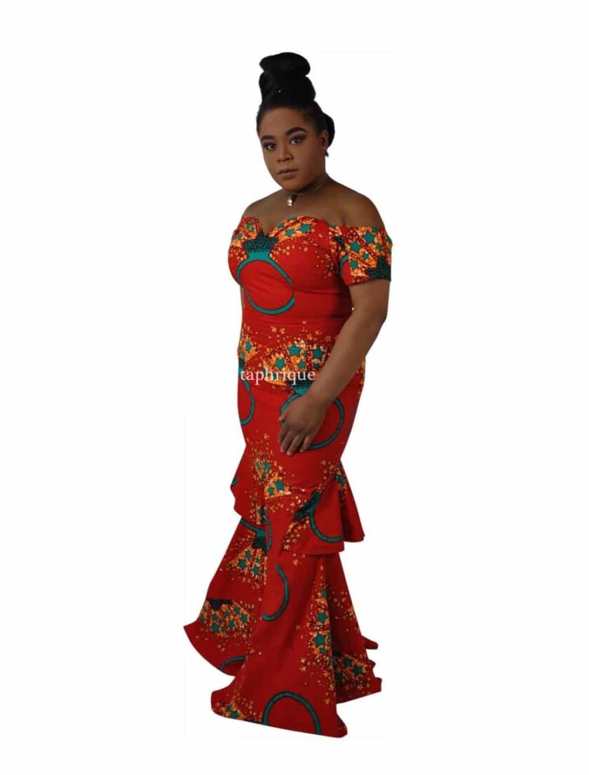 Side shot of model wearing a red off shoulder long fit and flare occasion dress with sweetheart neckline, front slit, peplum ruffles on the back in all over Ankara ring and star print.