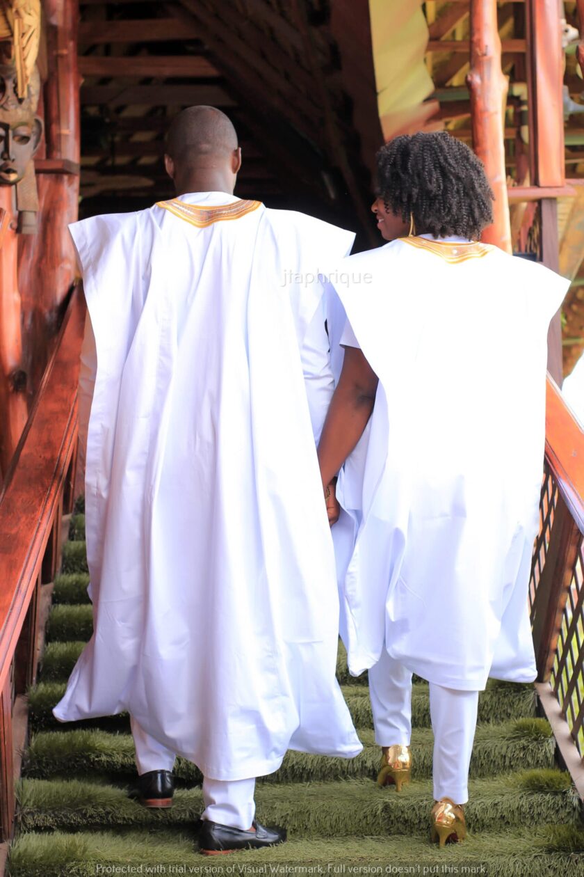 Back shot of male and female models wearing Mr & Mrs or his and hers matching traditional African suit outfits for couples, in white with gold embroidery. Perfect for a special occasion, wedding or Eid.