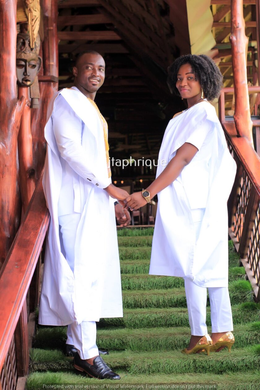 Side shot of male and female models wearing Mr & Mrs or his and hers matching traditional African suit outfits for couples, in white with gold embroidery. Perfect for a special occasion, wedding or Eid.