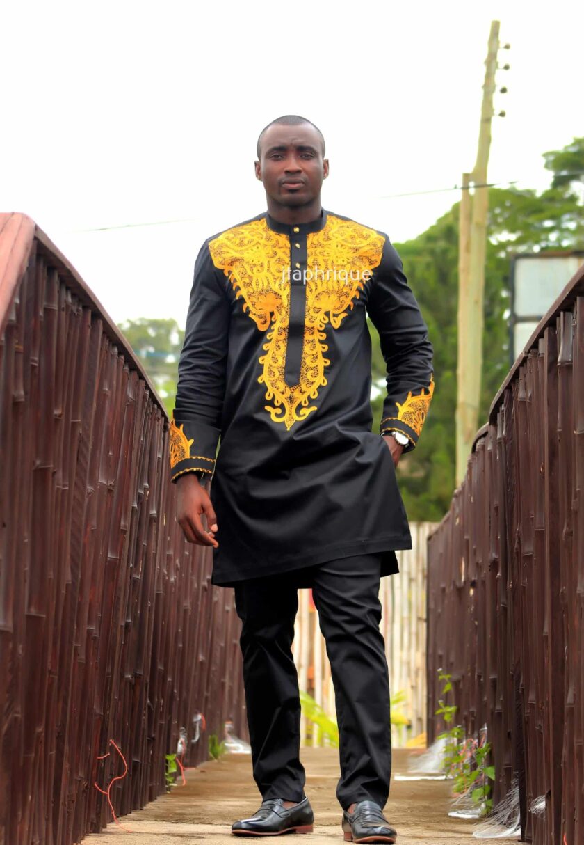 Full frontal of model wearing a solid black African senator suit with intricate gold embroidery on the neckline, chest, cuffs and back.