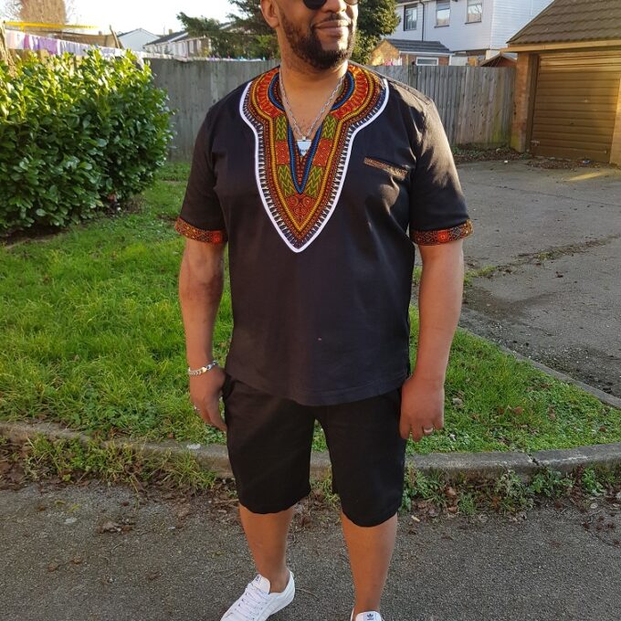 Full frontal of model wearing a solid black short sleeve Dashiki shirt with black shorts.