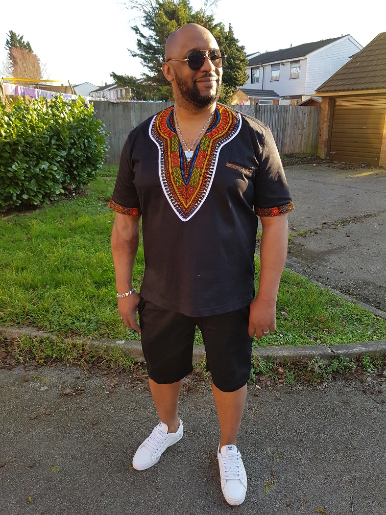 Full frontal of model wearing a solid black short sleeve Dashiki shirt with black shorts.