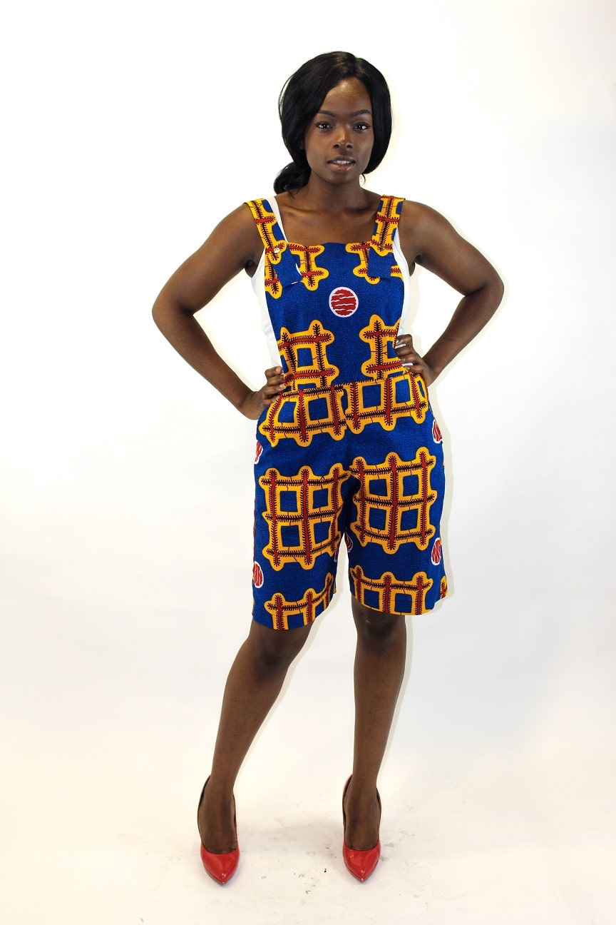 Frontal of model wearing a blue and multi-coloured Ankara pinafore playsuit in all over African print.