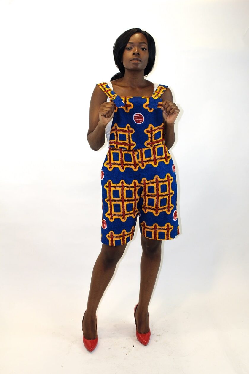 Frontal of model wearing a blue and multi-coloured Ankara pinafore playsuit in all over African print.