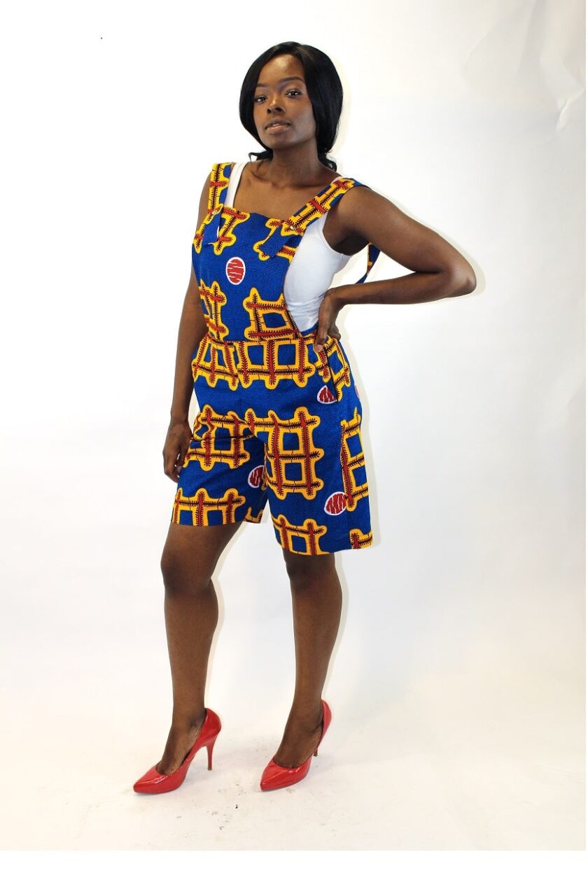 Side shot of model wearing a blue and multi-coloured Ankara pinafore playsuit in all over African print.