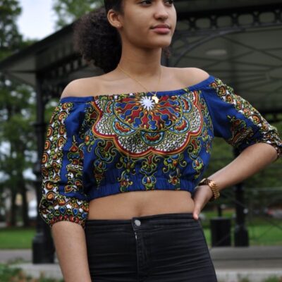 Frontal of model wearing a blue off shoulder boho crop top in all over African print pattern.