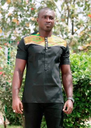 Close frontal of model wearing a solid black short sleeve shirt with vibrant multi-coloured Kente print across and above the chest to the neckline.