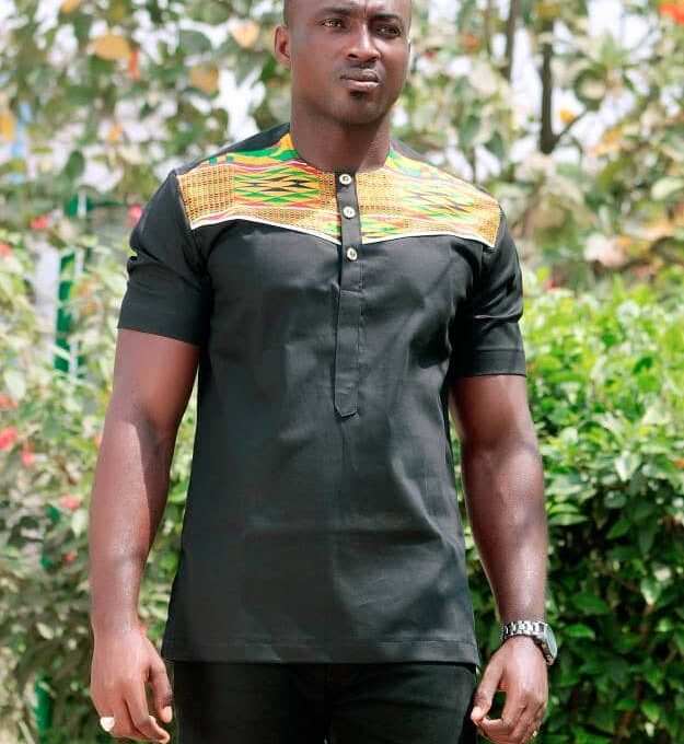 Close frontal of model wearing a solid black short sleeve shirt with vibrant multi-coloured Kente print across and above the chest to the neckline.