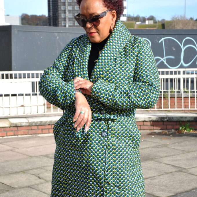 Frontal of model wearing a ladies green quilted coat in all over African Ankara print.