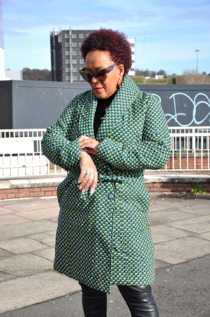 Frontal of model wearing a ladies green quilted coat in all over African Ankara print.