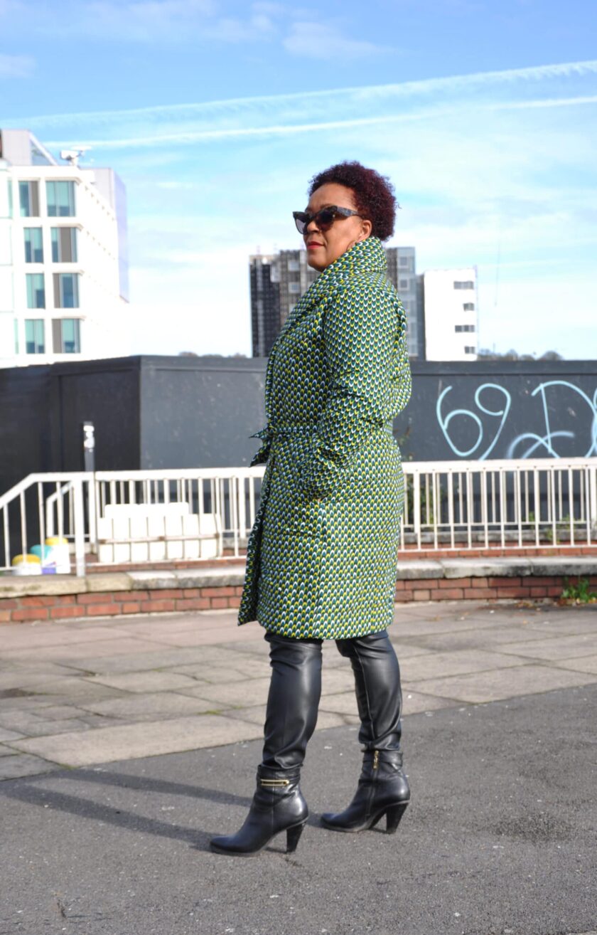 Side shot of model wearing a ladies green quilted coat in all over African Ankara print.