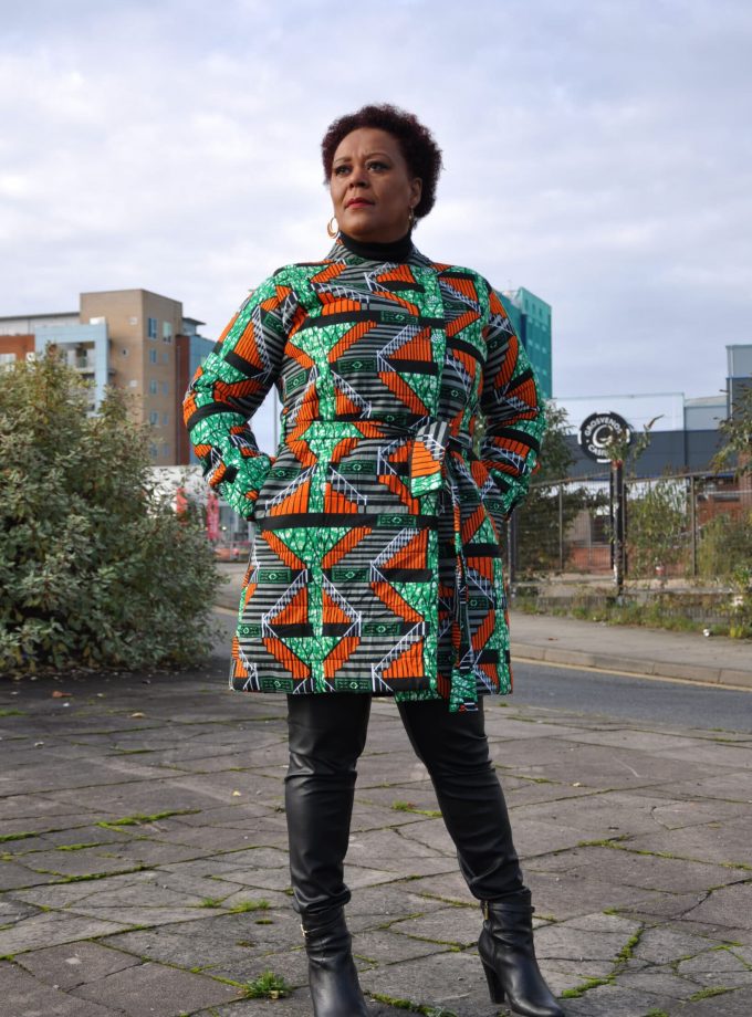 Frontal of model wearing a ladies quilted winter coat with green and orange multi-coloured all over African print.