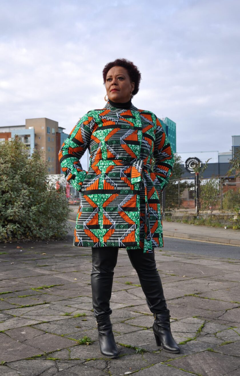 Frontal of model wearing a ladies quilted winter coat with green and orange multi-coloured all over African print.