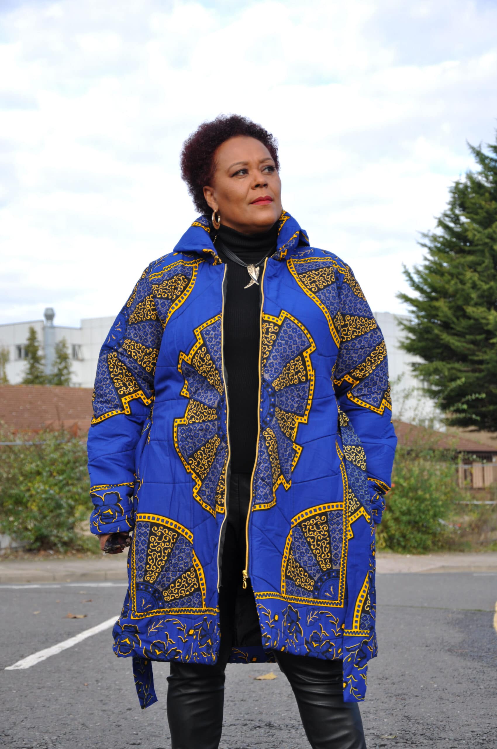 Frontal of model wearing a ladies African puffer coat in blue and gold Akufo Ankara all over print.