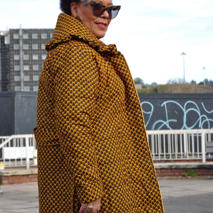 Side shot of model wearing a brown belted quilted ladies coat in all over African print.