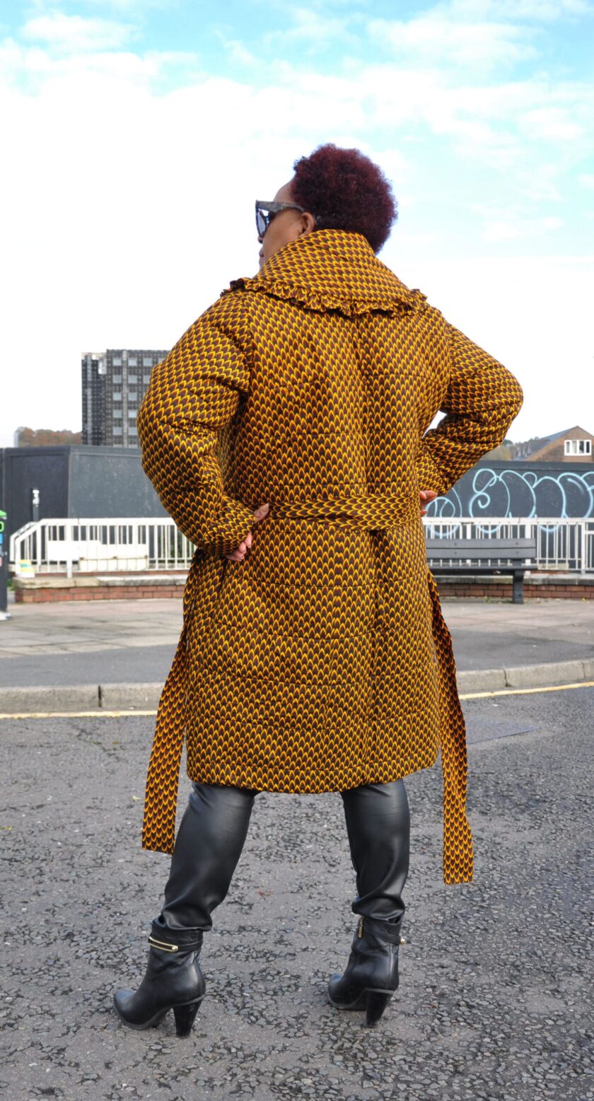 Back shot of model wearing a brown belted quilted ladies coat in all over African print.