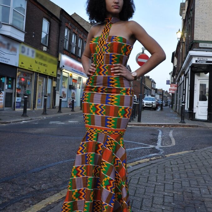 Full frontal of model wearing a halter silhouette flare dress fitted from top to thigh. Features all over vibrant colourful African print.