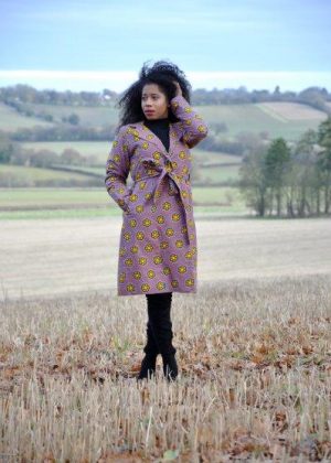 Full frontal of model wearing a ladies belted trench coat in lilac and all over African print.