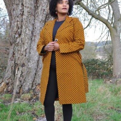 Full frontal of model wearing a mustard ladies trench coat in all over African Ankara print.