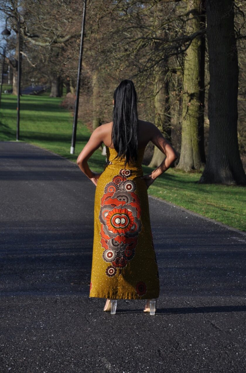 Back shot of model wearing a long strapless cream lace and mustard yellow Ankara fit and flare dress with African print rosette detail on the skirt.