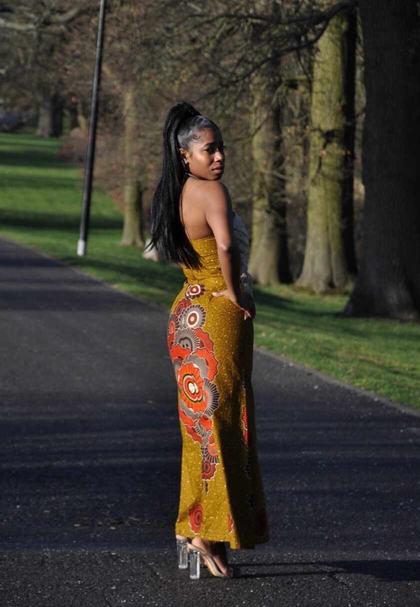 Side shot of model wearing a long strapless cream lace and mustard yellow Ankara fit and flare dress with African print rosette detail on the skirt.