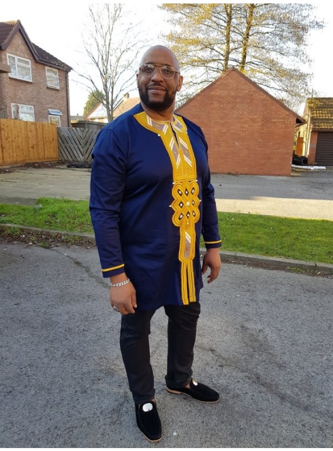 Full frontal of model wearing a men's navy blue longline shirt embroidered with gold African embroidery detail on neckline, chest and cuffs.