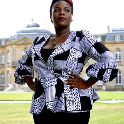 Frontal of model wearing a ladies white and black peplum top in all over graphic African print.