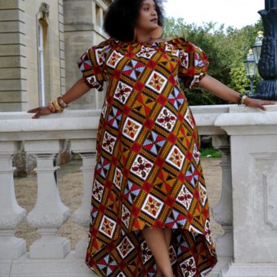Frontal of model wearing a gold coloured maxi dress with high-low asymmetrical hem, off shoulder neckline, short puff sleeves in all over multi-coloured African print pattern.