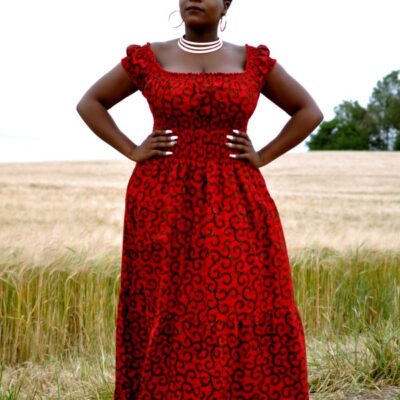 Full frontal of model wearing a cap sleeve red maxi dress in all over swirly African Ankara print.