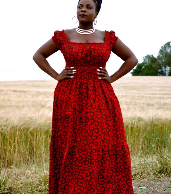 Full frontal of model wearing a cap sleeve red maxi dress in all over swirly African Ankara print.