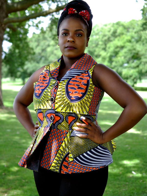 Close shot of model wearing a colourful sleeveless peplum top with yellow, orange and green all over African Ankara print pattern.