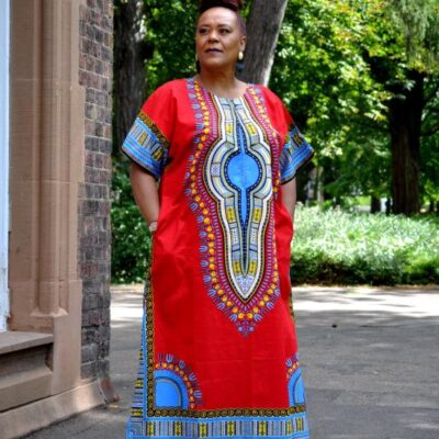Full frontal of model wearing a red & multi-coloured dashiki print kaftan dress in maxi length.