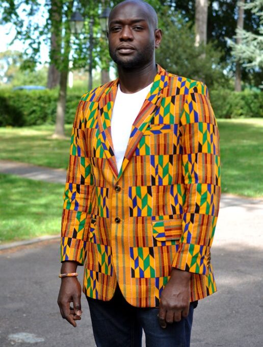 Frontal of model wearing a men's single breasted blazer in vibrant, colourful all over African Kente print pattern.