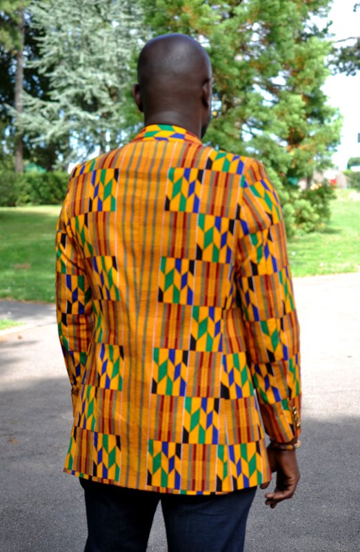 Back shot of model wearing a men's single breasted blazer in vibrant, colourful all over African Kente print pattern.