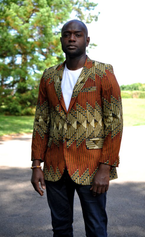 Frontal of model wearing a men's single breasted blazer in brown, green and cream, multi-coloured all over African Ankara print pattern.