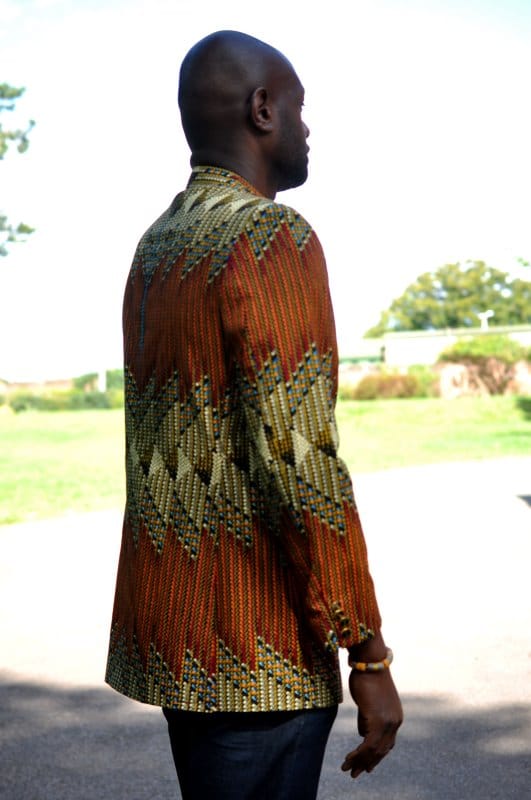 Side shot of model wearing a men's single breasted blazer in brown, green and cream, multi-coloured all over African Ankara print pattern.
