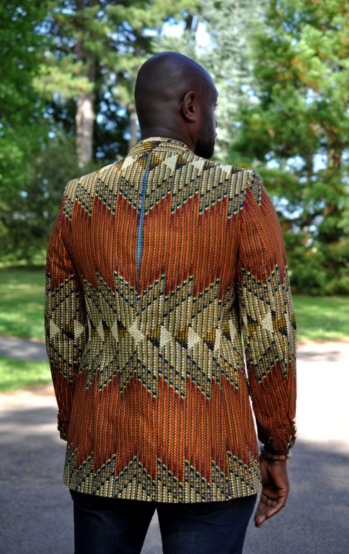 Back shot of model wearing a men's single breasted blazer in brown, green and cream, multi-coloured all over African Ankara print pattern.