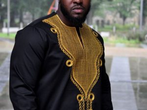 Frontal of model wearing a traditional African black shirt with gold embroidery.