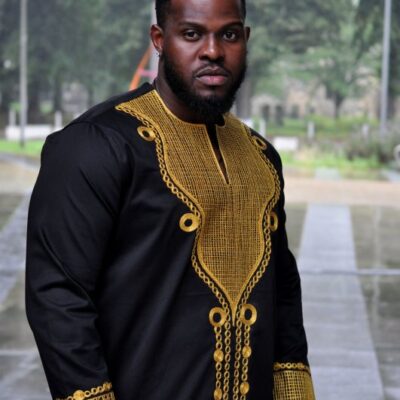 Frontal of model wearing a traditional African black shirt with gold embroidery.