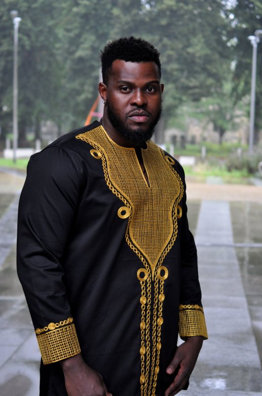 Frontal of model wearing a traditional African black shirt with gold embroidery.