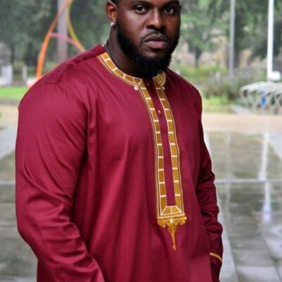Frontal of model wearing a maroon traditional African shirt with gold panel embroidery on the front and neckline.