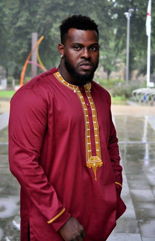 Frontal of model wearing a maroon traditional African shirt with gold panel embroidery on the front and neckline.