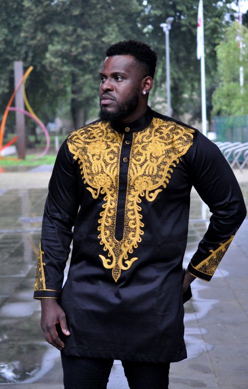 Frontal of model wearing a traditional black African shirt with intricate gold embroidery on the front and sleeves.