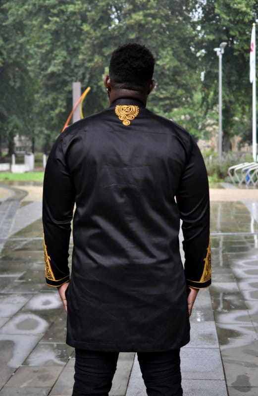 Back shot of model wearing a traditional black African shirt with intricate gold embroidery on the back neckline and sleeves.