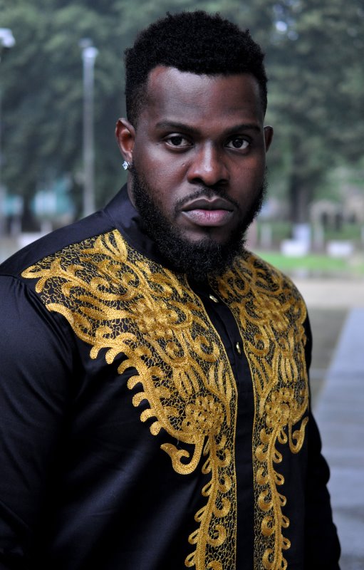 Close shot of model wearing a traditional black African shirt with intricate gold embroidery on the front.