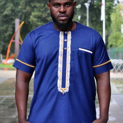 Frontal of model wearing a short sleeve blue African shirt with white and gold panel embroidery detail on the chest and gold embroidery detail on the sleeves.
