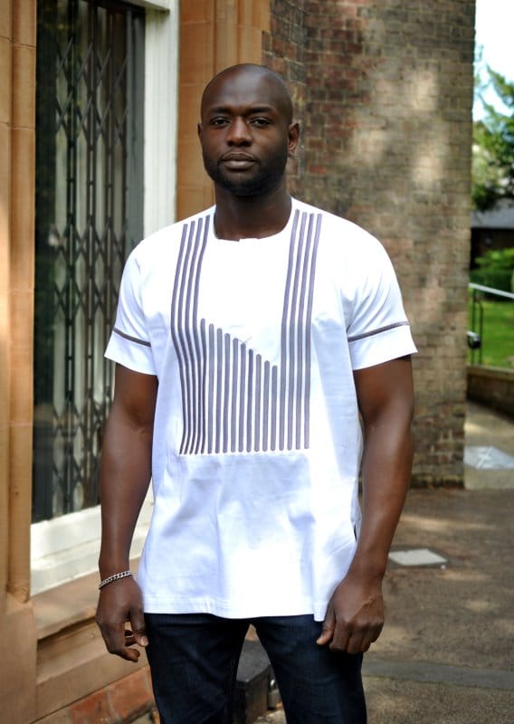 Frontal of model wearing a white short sleeved traditional African shirt with ash grey striped embroidery on front and sleeves.