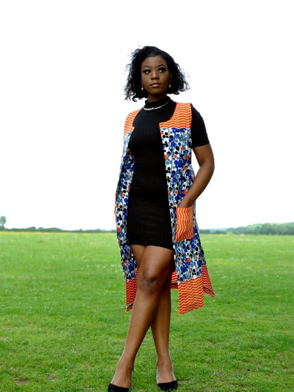 Full frontal of model wearing a ladies open front trench vest in all over colourful African print.
