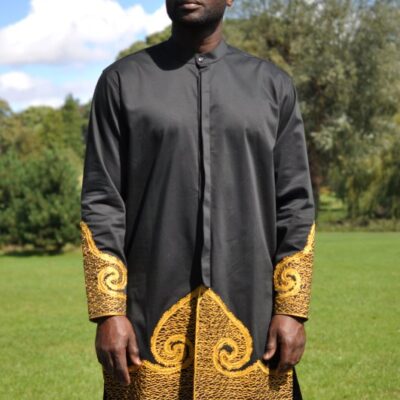 Frontal of model wearing a long black traditional African shirt with gold embroidery.